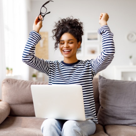 Woman with medium-dark skin tone celebrates reading job acceptance email on her laptop